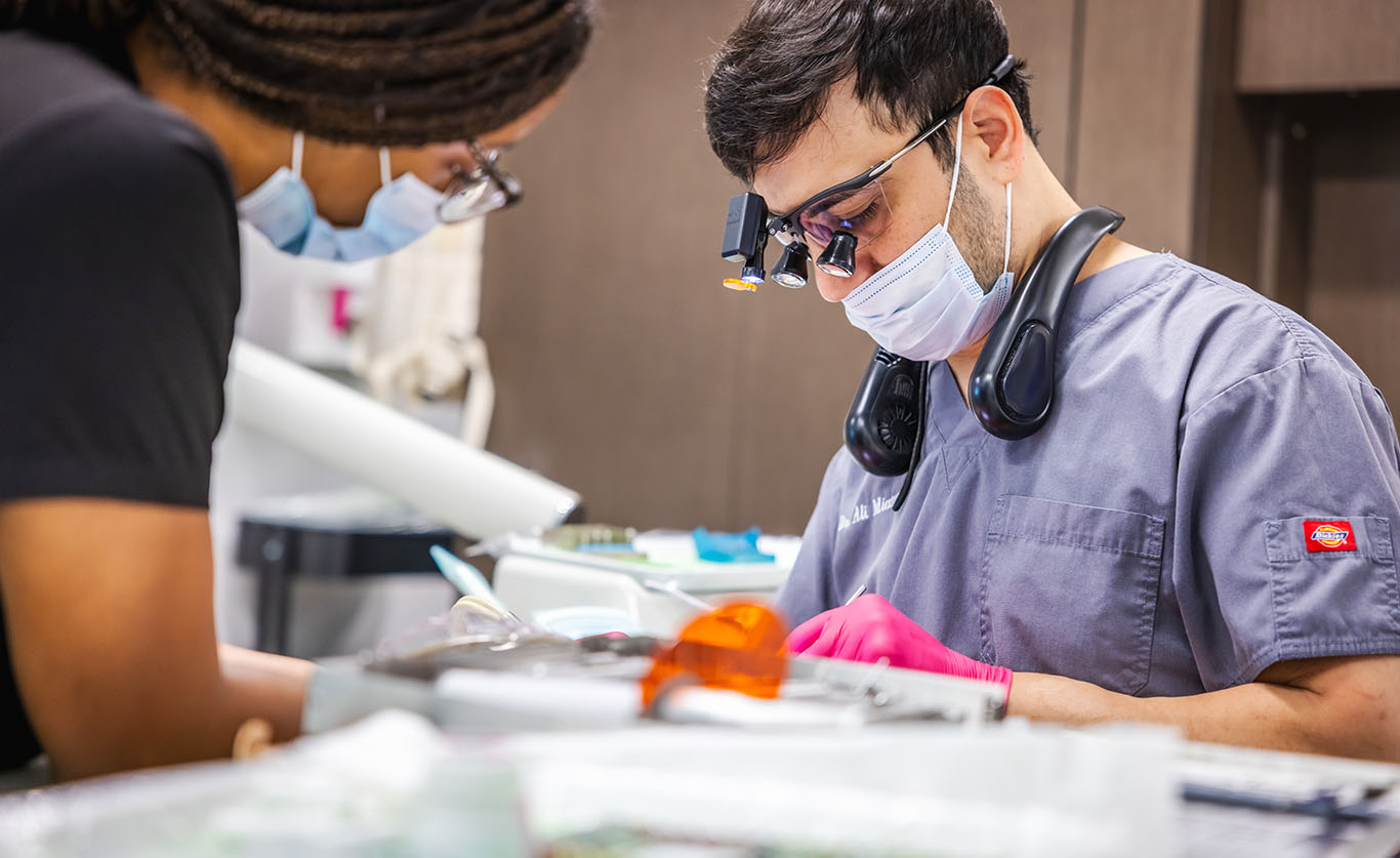 a man in a hospital mask is cutting a piece of paper  at cosmetic dentistry in Reston, VA